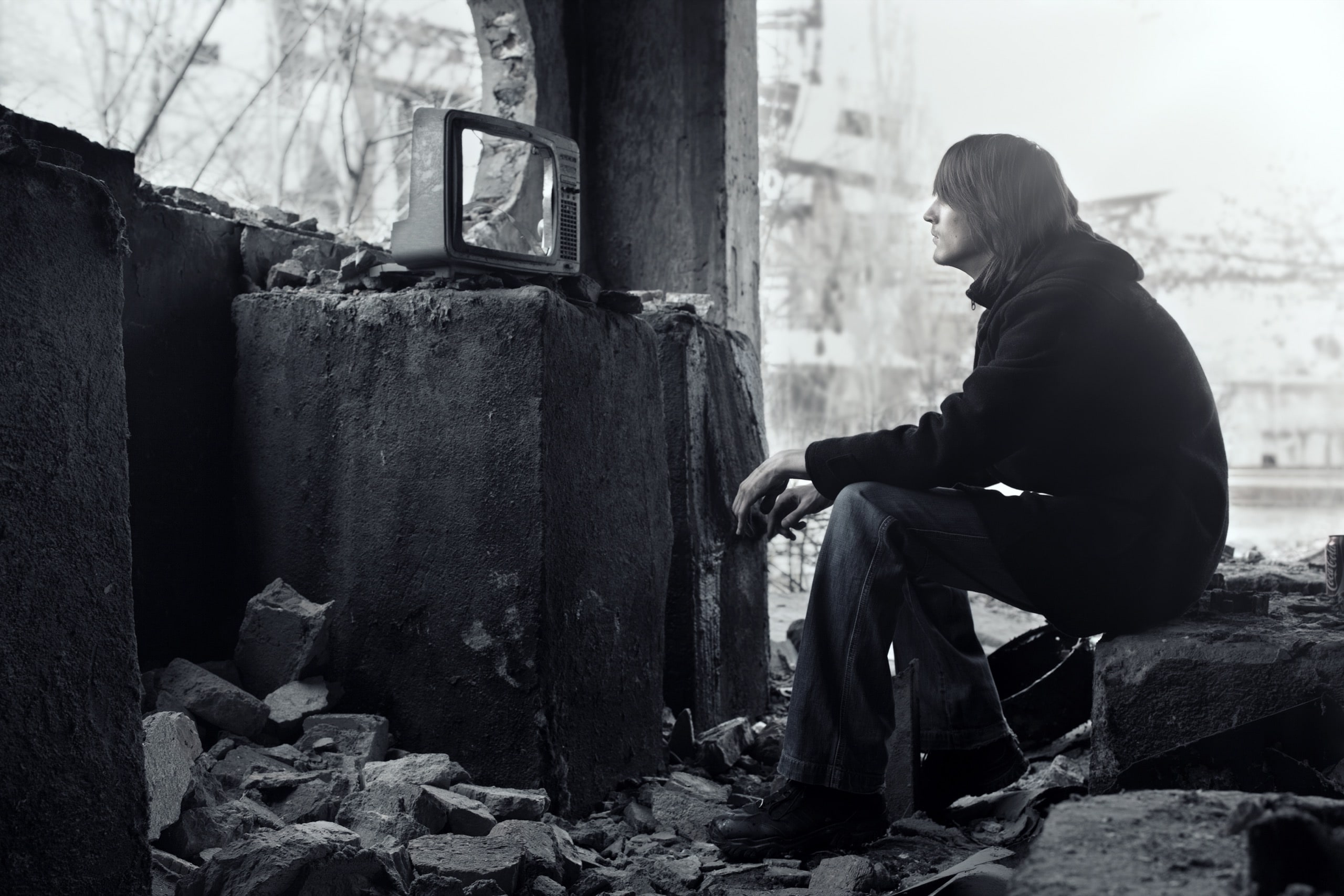 Homeless man watching broken TV-set in the ruined interior. Shallow depth of field due to the tilt lens for movie effect